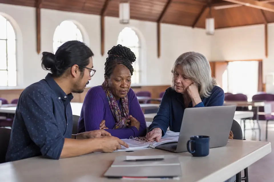 Three nonprofit founders reviewing incorporation papers and a laptop in a fellowship hall