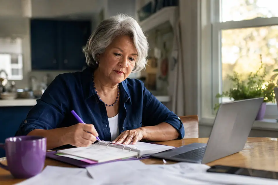 Volunteer nonprofit treasurer reviewing a planner and laptop at a home kitchen table