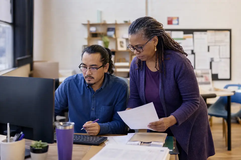 Two nonprofit staff members reviewing financial statements at a community center office computer