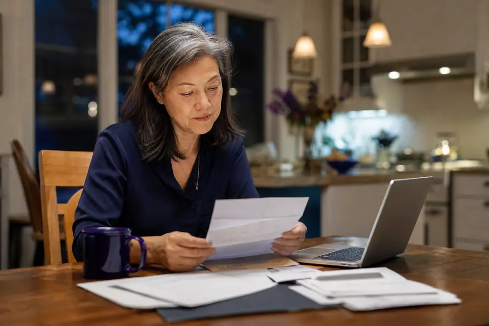 Board treasurer at home reviewing mail and a laptop at a kitchen table