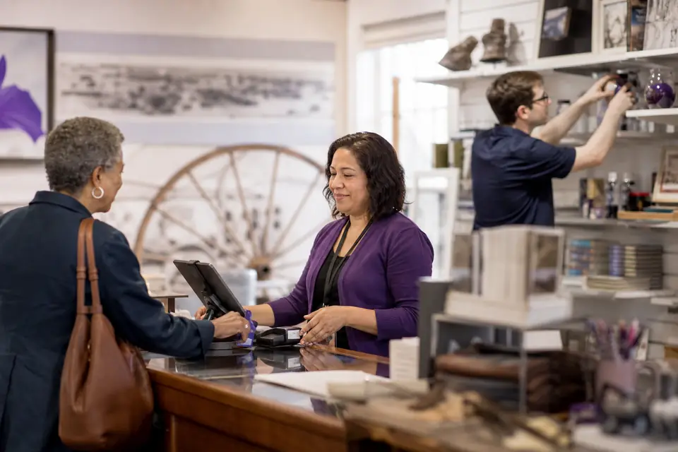 Volunteer at a small museum gift shop counter with a staff member restocking